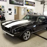 black muscle car with white racing stripes on hood in detailing shop